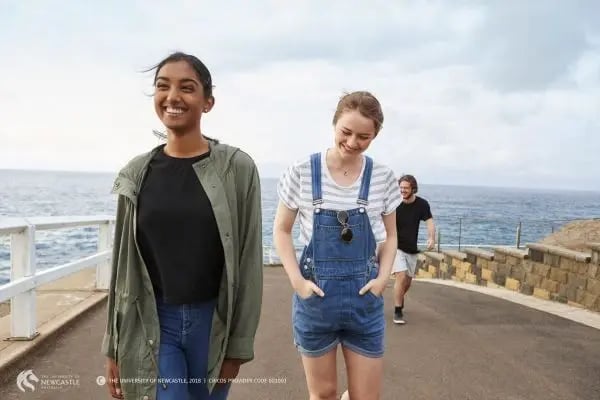 Zwei Studierende der University of Newcastle laufen lächelnd am Meer entlang
