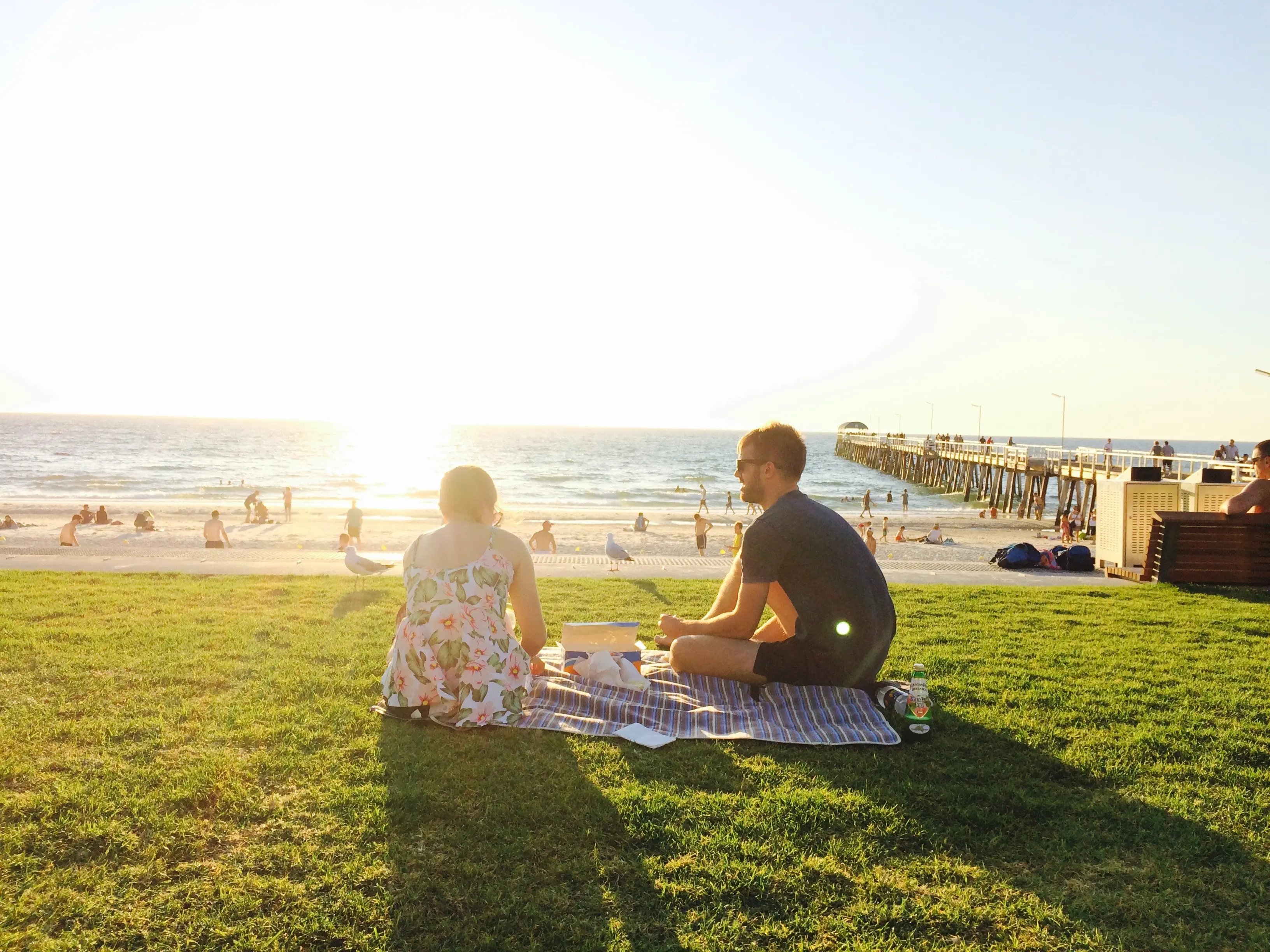 Zwei Studierende genießen ein Picknick am Strand bei Sonnenuntergang in Australien – Auslandssemester mit Urlaubsfeeling.