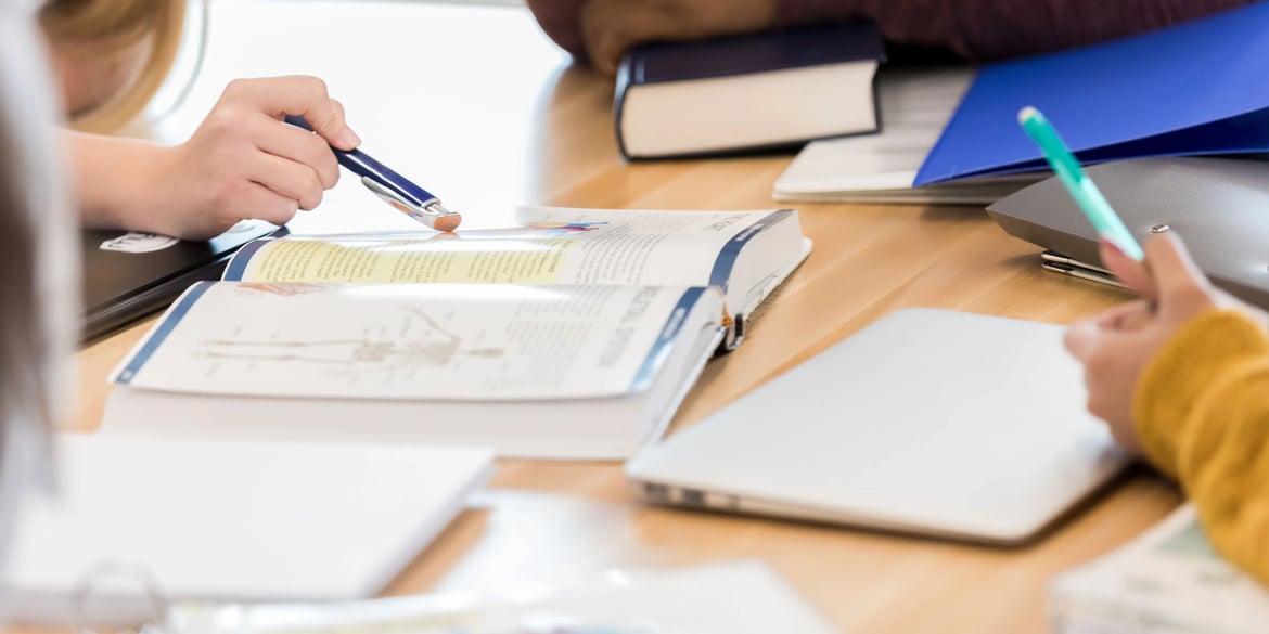 Studierende arbeiten gemeinsam an einem Tisch mit geöffneten Lehrbüchern, Notizblöcken und Laptops – typische Lernsituation im Auslandssemester.