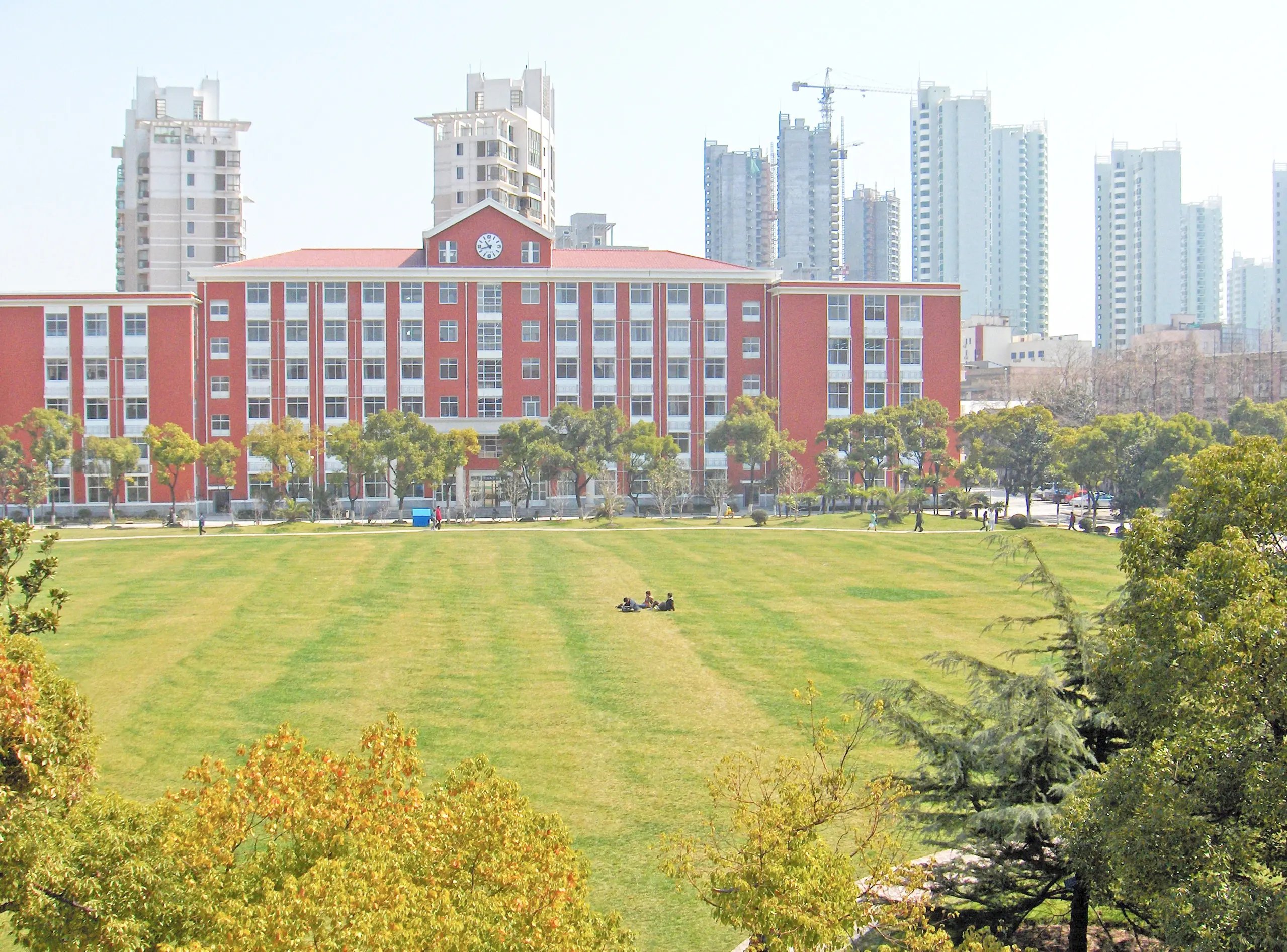Campus der Shanghai University mit grüner Rasenfläche und Stadtpanorama im Hintergrund.