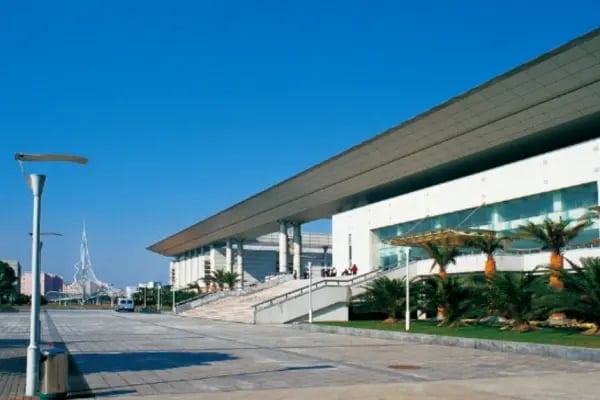 Ein modernes Studiengebäude der Shanghai University vor blauem Himmel mit breiter Treppe und grüner Umgebung.