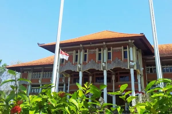 Traditionelles Gebäude mit rotem Dach und indonesischer Flagge auf dem Campus der Udayana University.