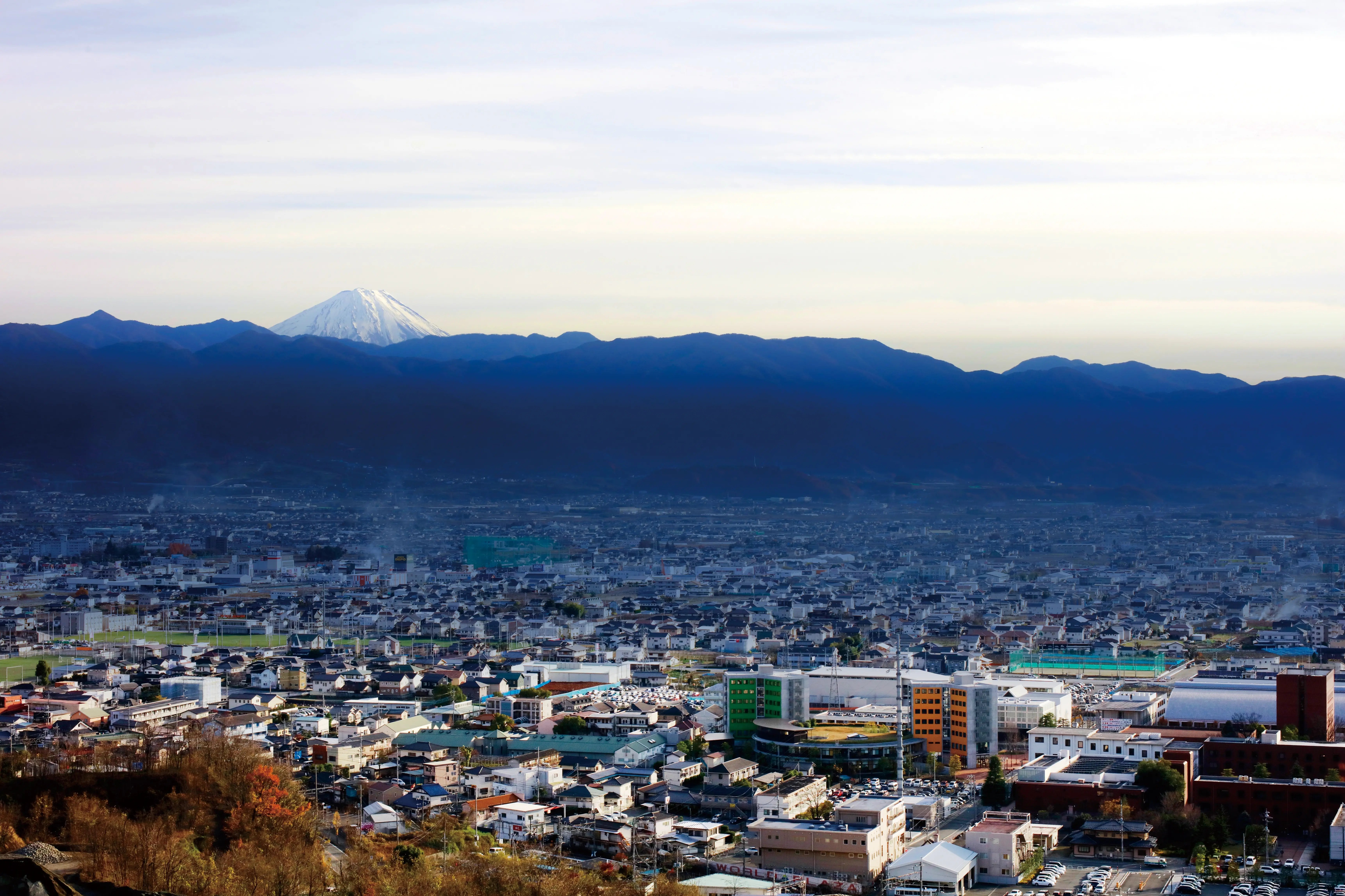 Vogelperspektive der Stadt Kofu und des Campus der Yamanashi Gaukin University mit Bergen im Hintergrund.