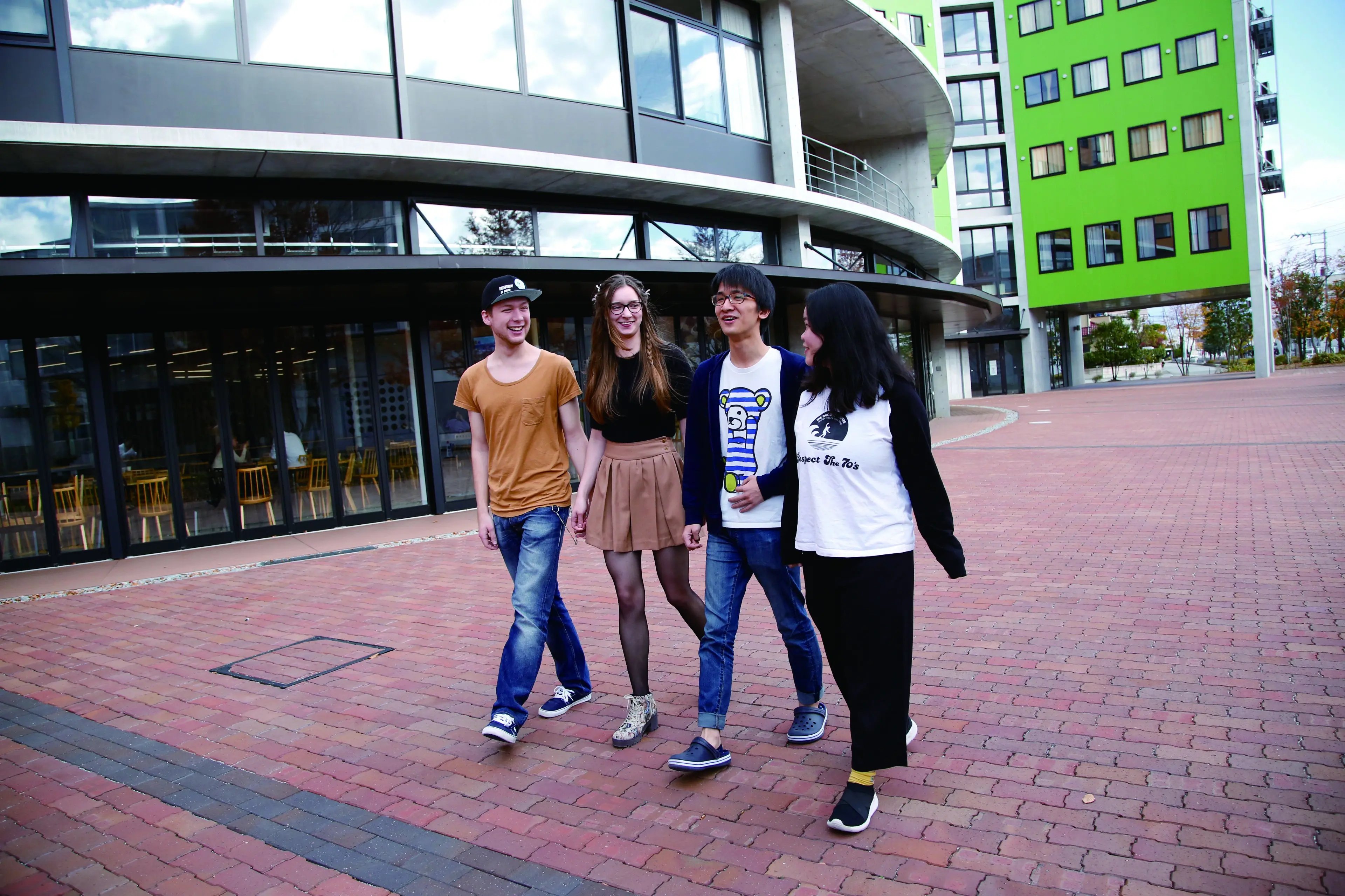 Vier Studierende laufen am Campus der Yamanashi Gaukin University entlang.
