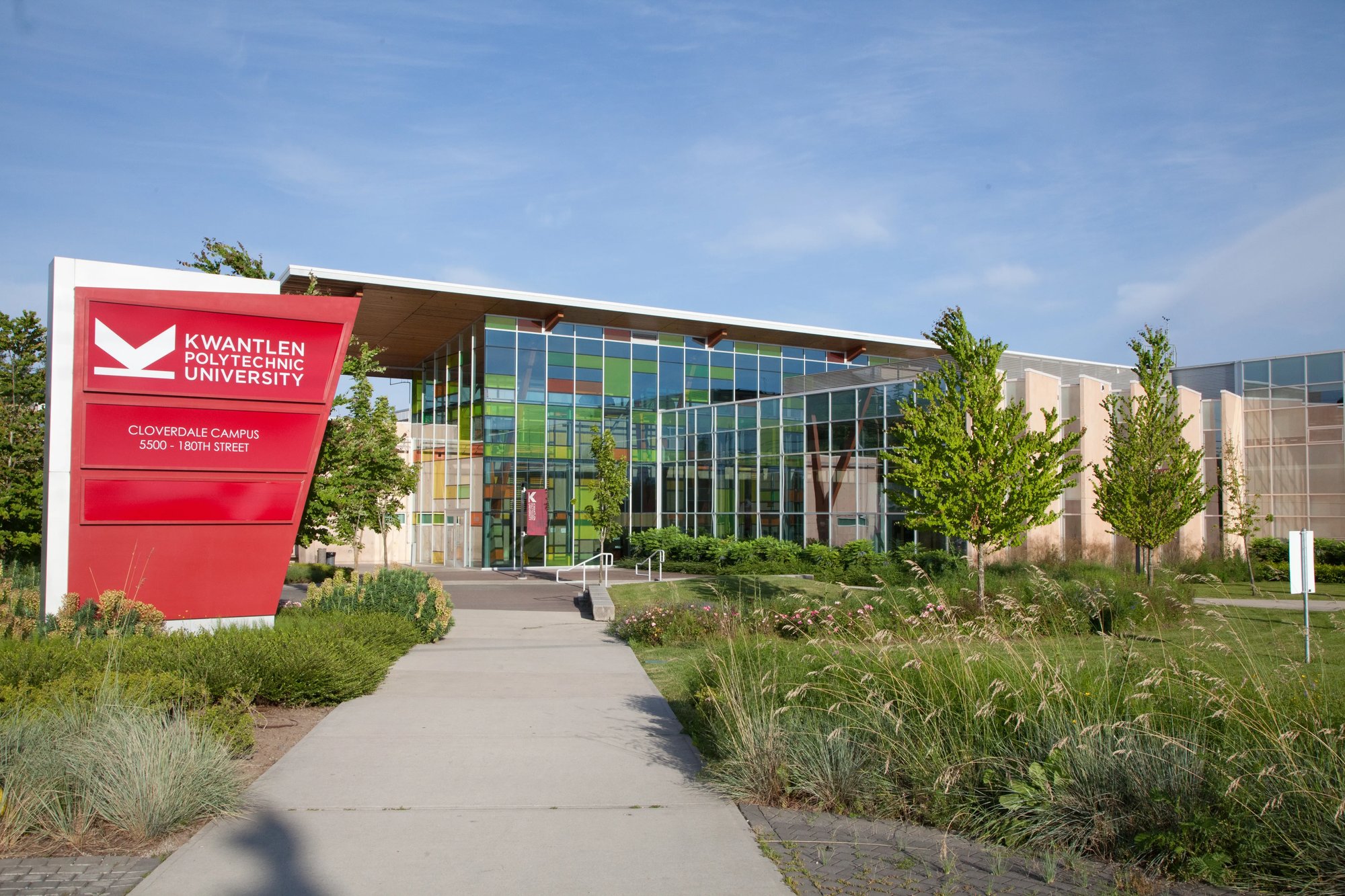 Grüner Campus der Kwantlen Polytechnic University mit Glasgebäude und rotem Banner.