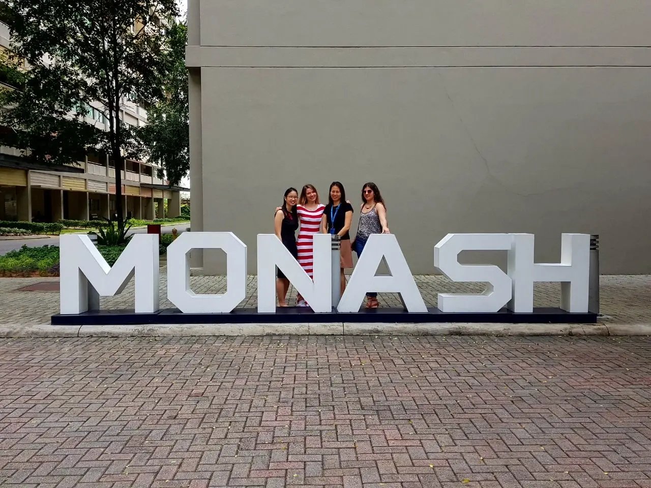 4 Studierende stehen am Campus hinter dem Schild der Monash University Malaysia.