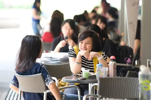 Zwei Studentinnen der Monash University Malaysia unterhalten sich an einem Tisch.