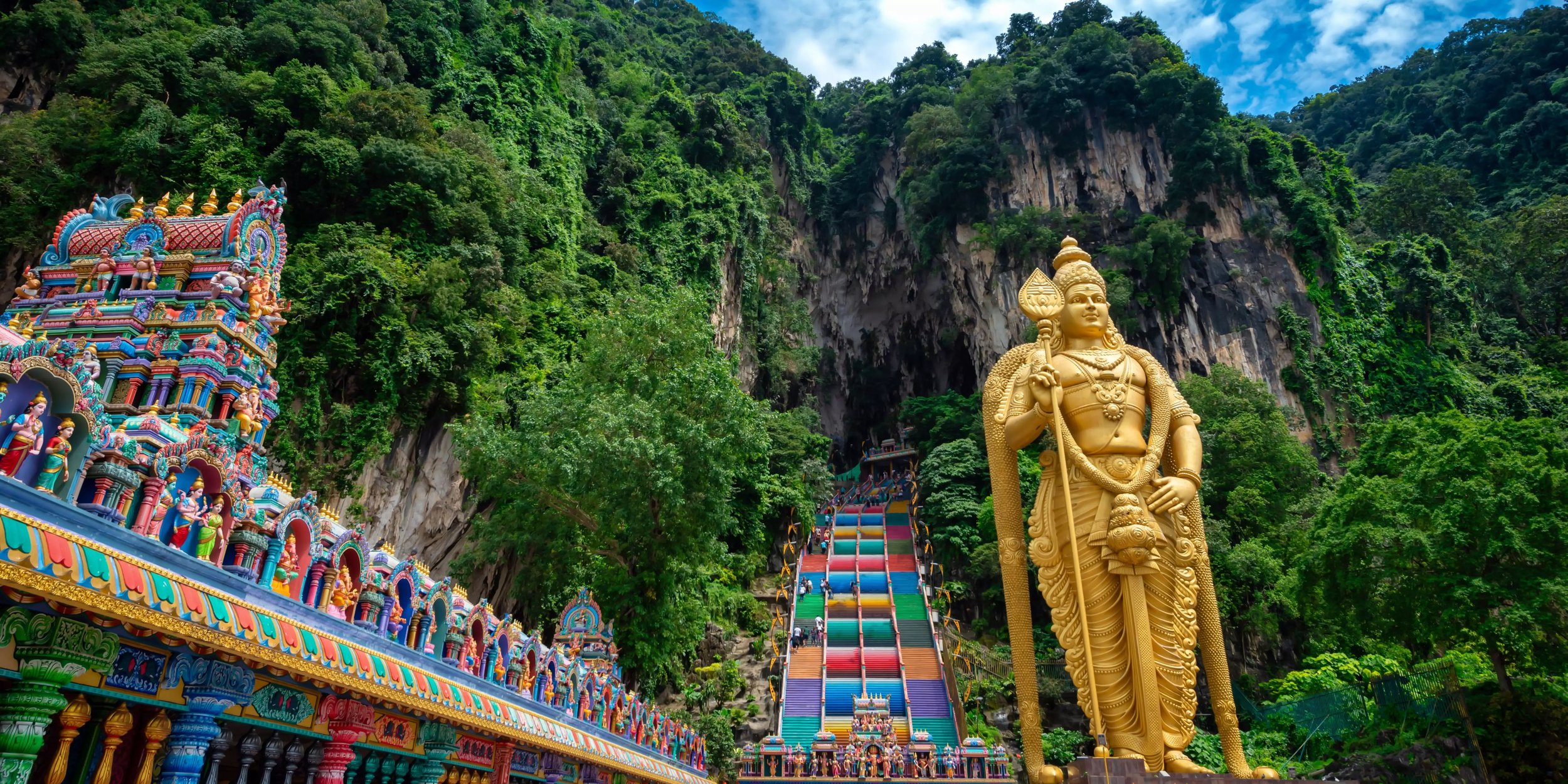 Die berühmten Batu Caves in Malaysia mit ihrer bunten Tempelanlage und der goldenen Statue des Gottes Murugan im Vordergrund.