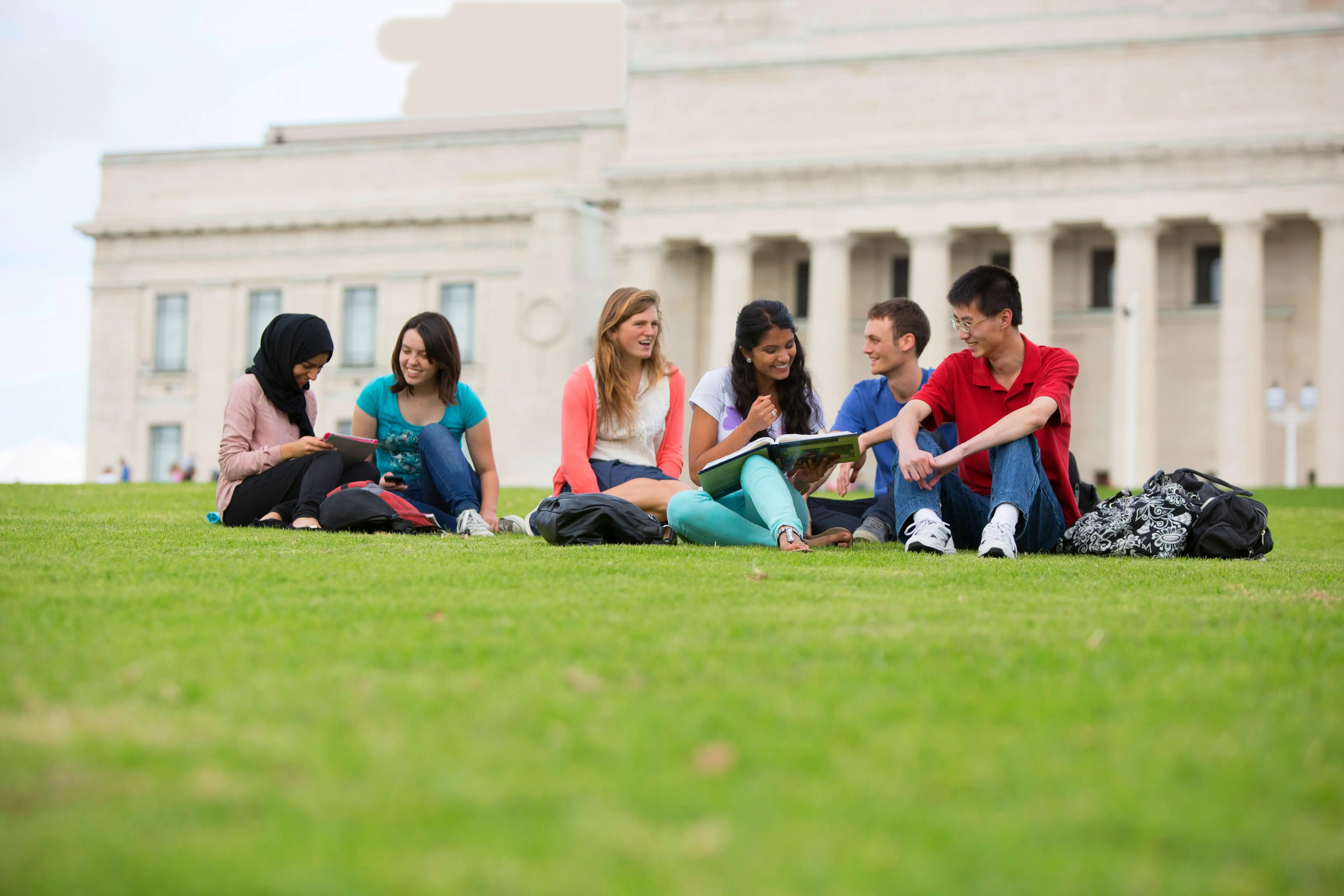 Eine Gruppe Studierende sitzen auf einer Grünfläche vor dem Campus der University of Auckland