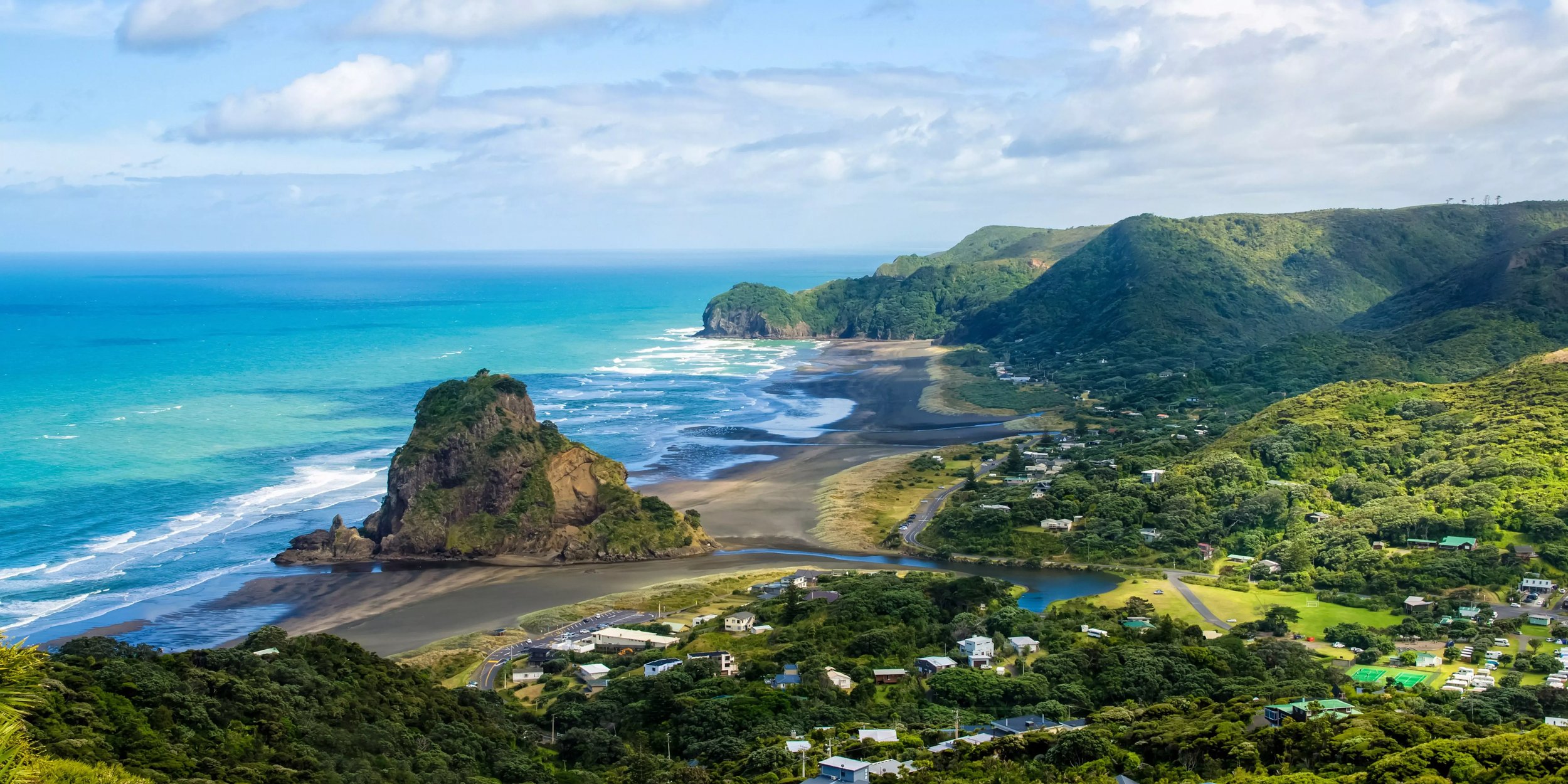 Küstenlandschaft in Neuseeland mit einer grünen, felsigen Landzunge, die ins Meer ragt. 