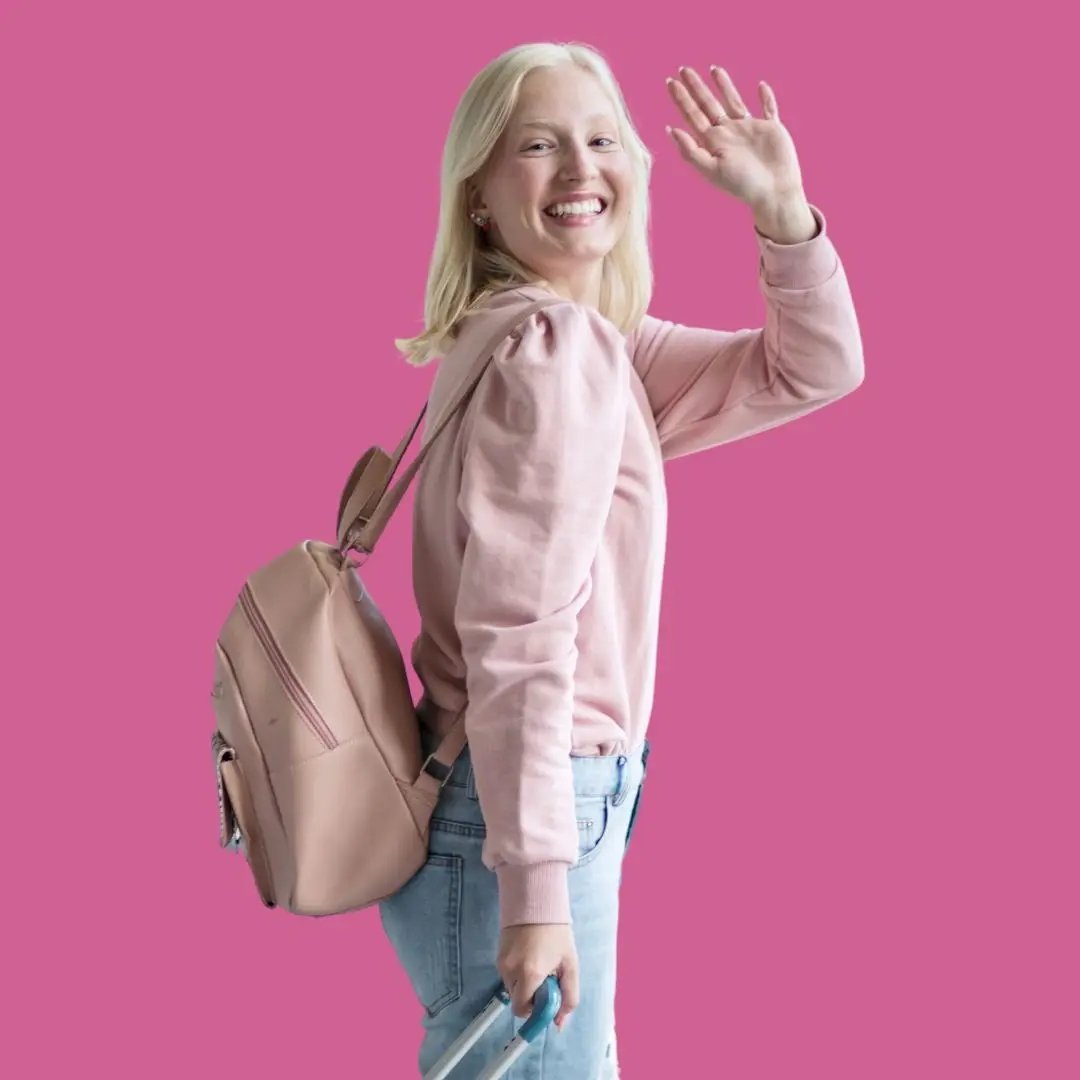 Junge Studentin mit Rucksack winkt fröhlich – bereit für ihr Auslandssemester voller Abenteuer. 