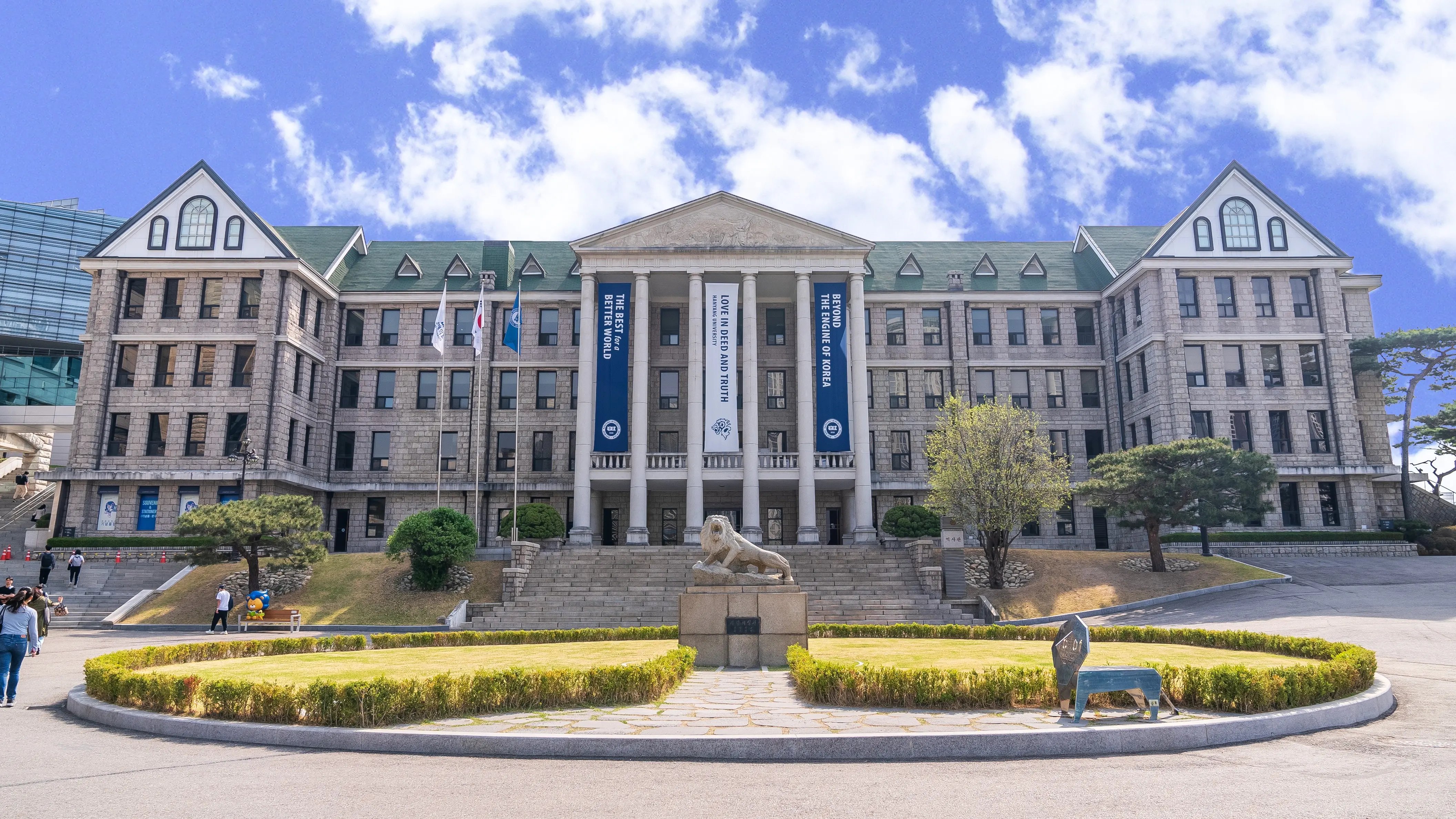 Historisches Hauptgebäude der Hanyang University mit Löwenskulptur im Vordergrund und blauem Himmel 