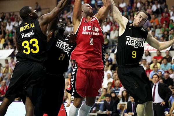 Drei Basketballspieler der Universidad Católica de Murcia springen beim Spiel 