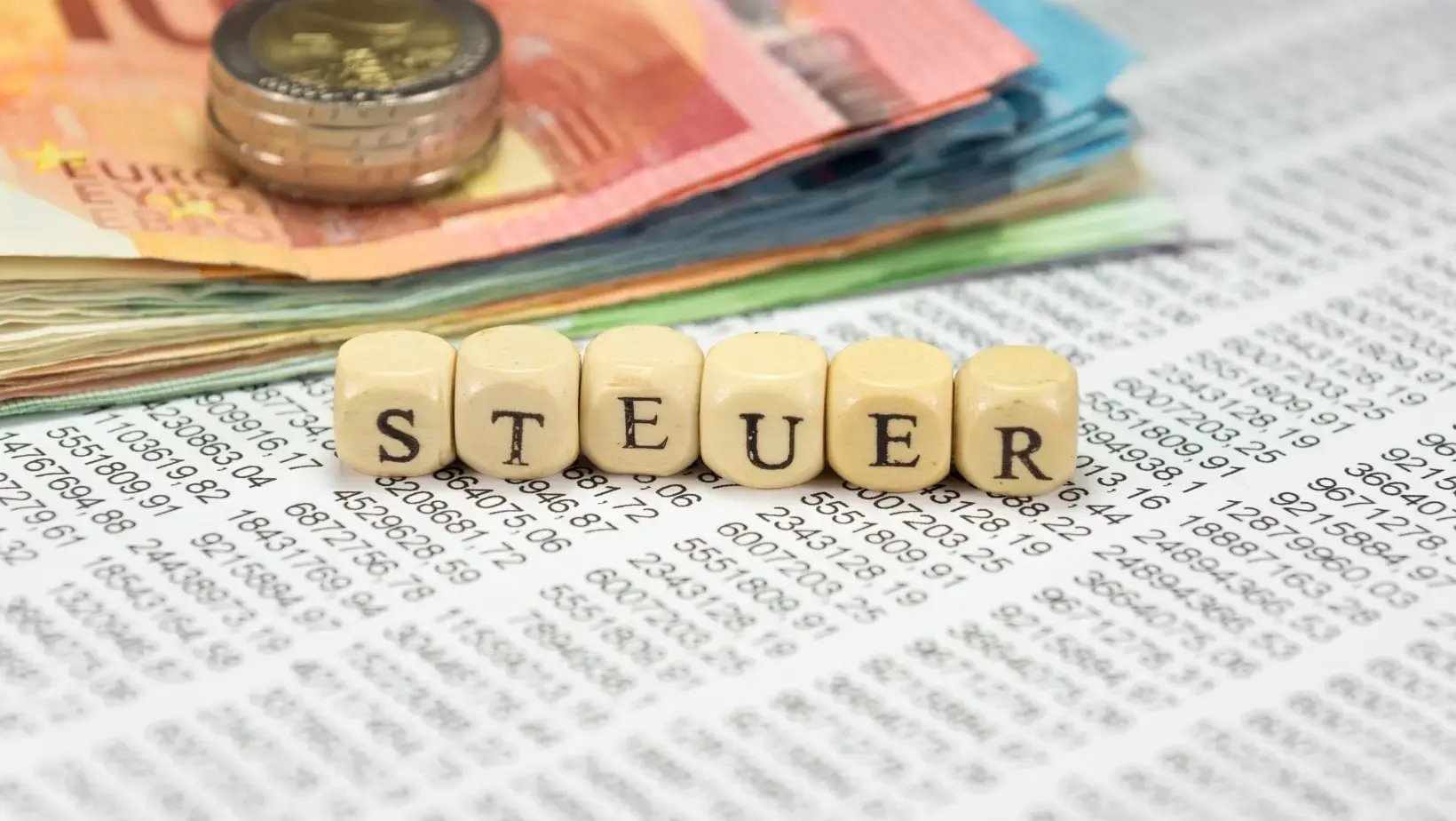 Holzwürfel bilden das Wort 'Steuer' vor Geldscheinen und Münzen auf Finanzdokumenten. 
