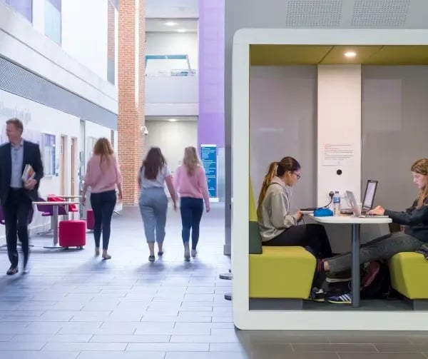 Studierende an der University of Sussex: Zwei Personen arbeite in einer modernen Lernlounge, andere laufen durch den Campusbereich