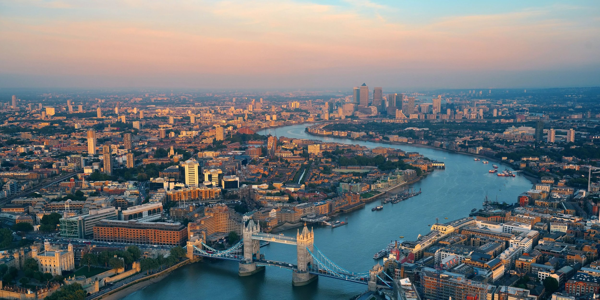 Luftaufnahme von London mit der Tower Bridge und der Themse bei Sonnenuntergang. Skyline der Stadt mit Canary Wharf im Hintergrund – ikonische Sehenswürdigkeiten und Architektur.