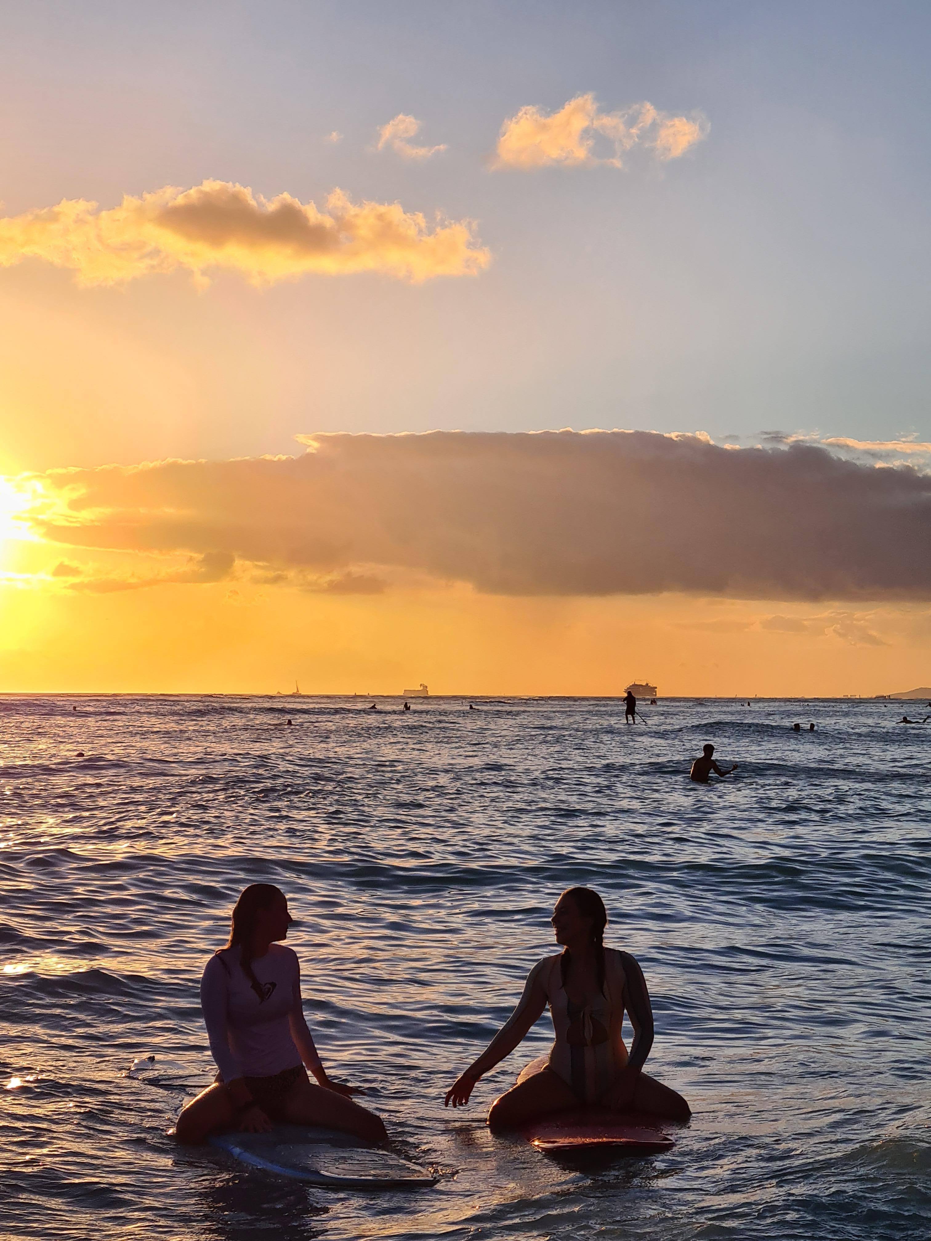 Zwei Frauen sitzen auf Surfbrettern im Meer während des Sonnenuntergangs 