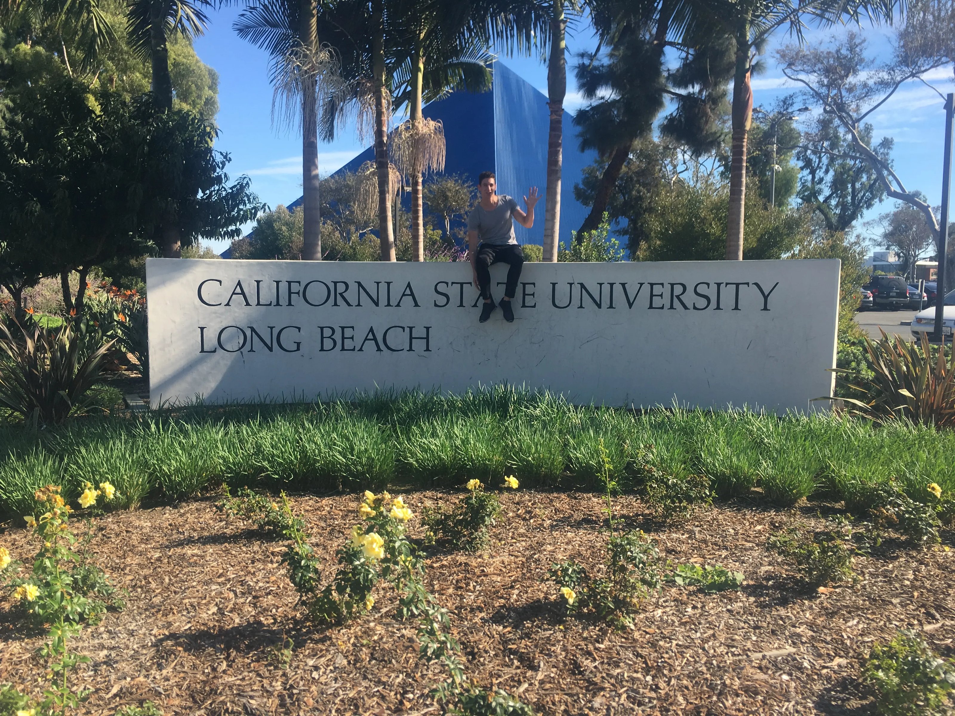 Ein Student sitzt auf dem Universitätsschild der California State University, Long Beach