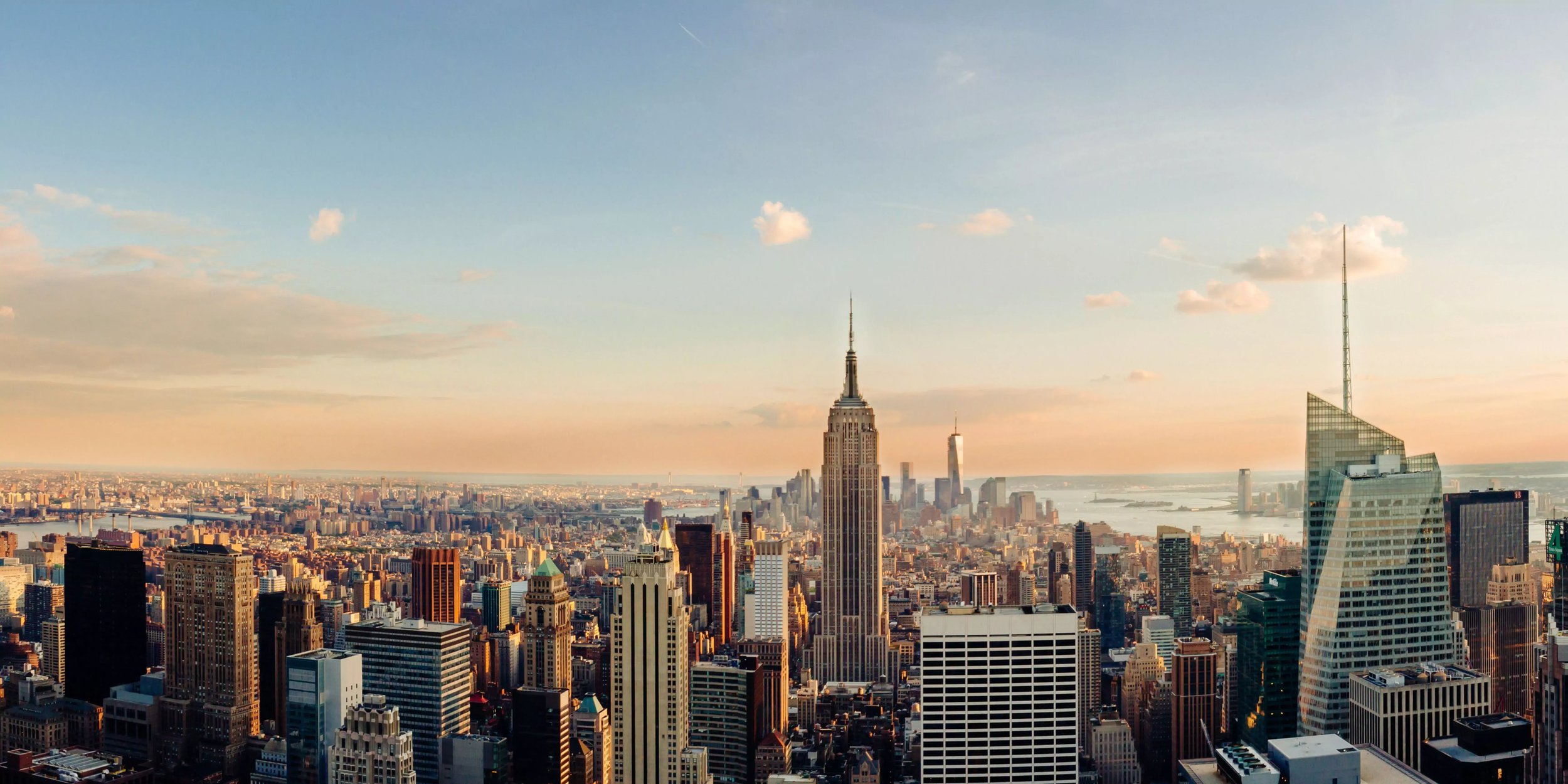 Skyline von New York City mit dem Empire State Building im Vordergrund bei Sonnenuntergang.