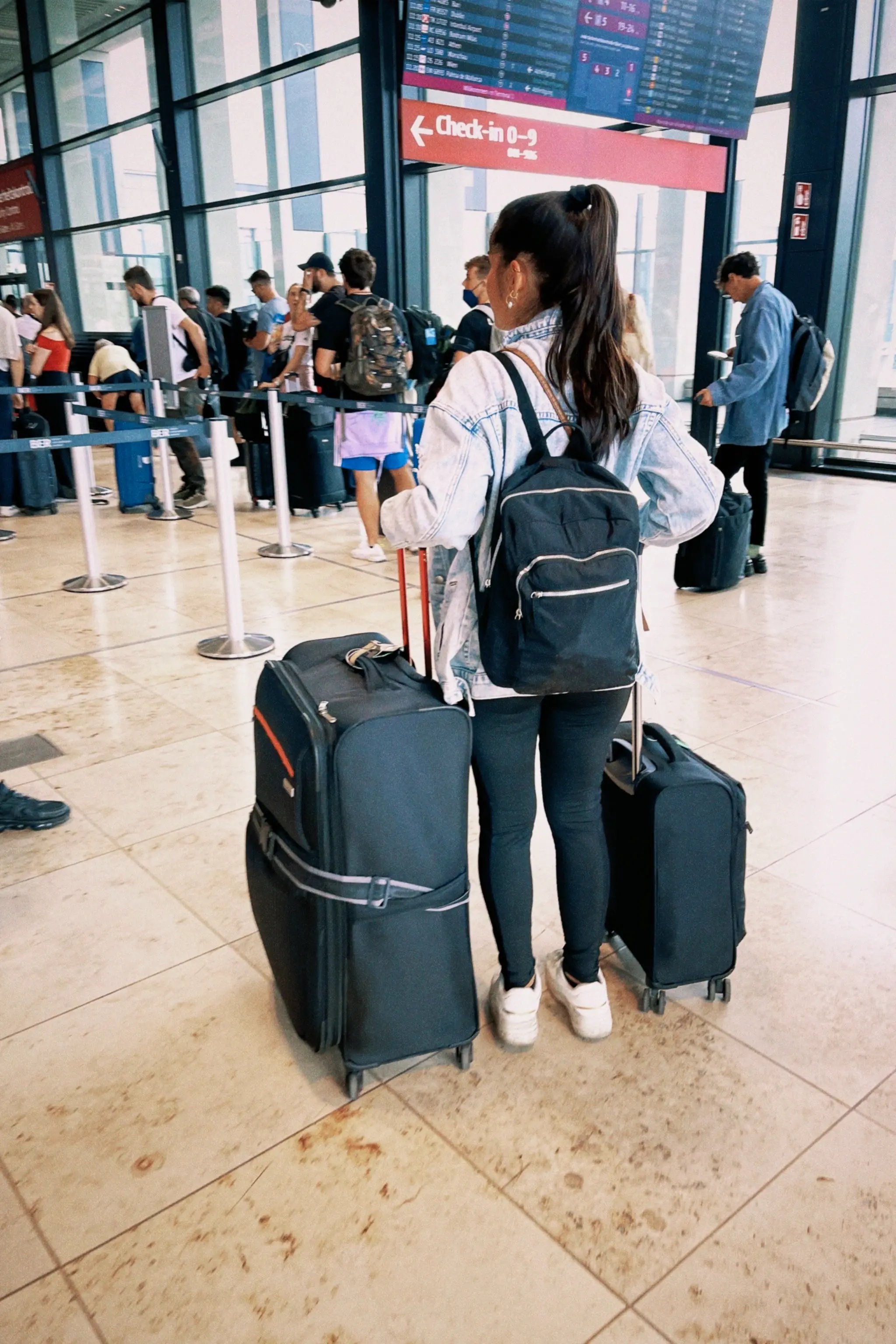 Reisende mit Rucksack und zwei Koffern steht am Flughafen in einer Warteschlange