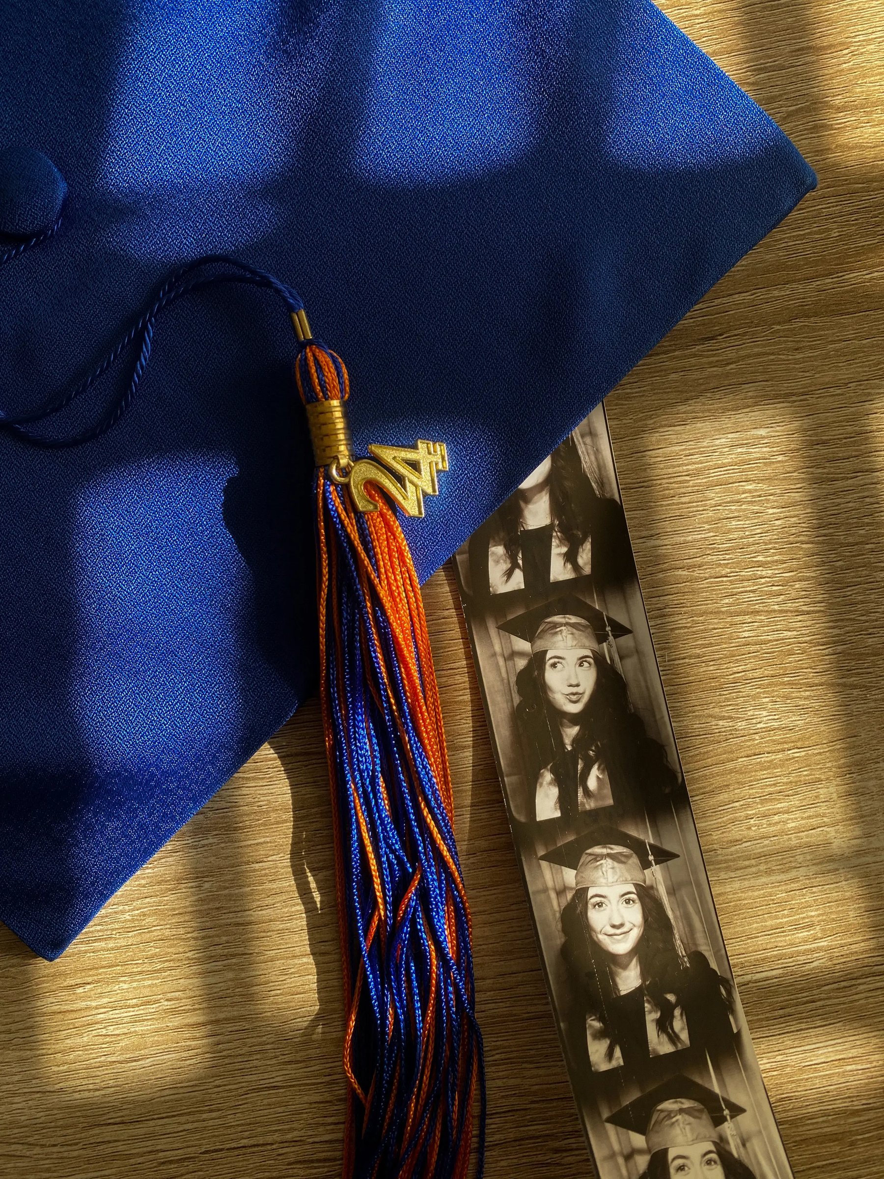 Blauer Doktorhut mit bunter Quaste und Fotostreifen auf Holztisch, symbolisiert Studienabschluss. 